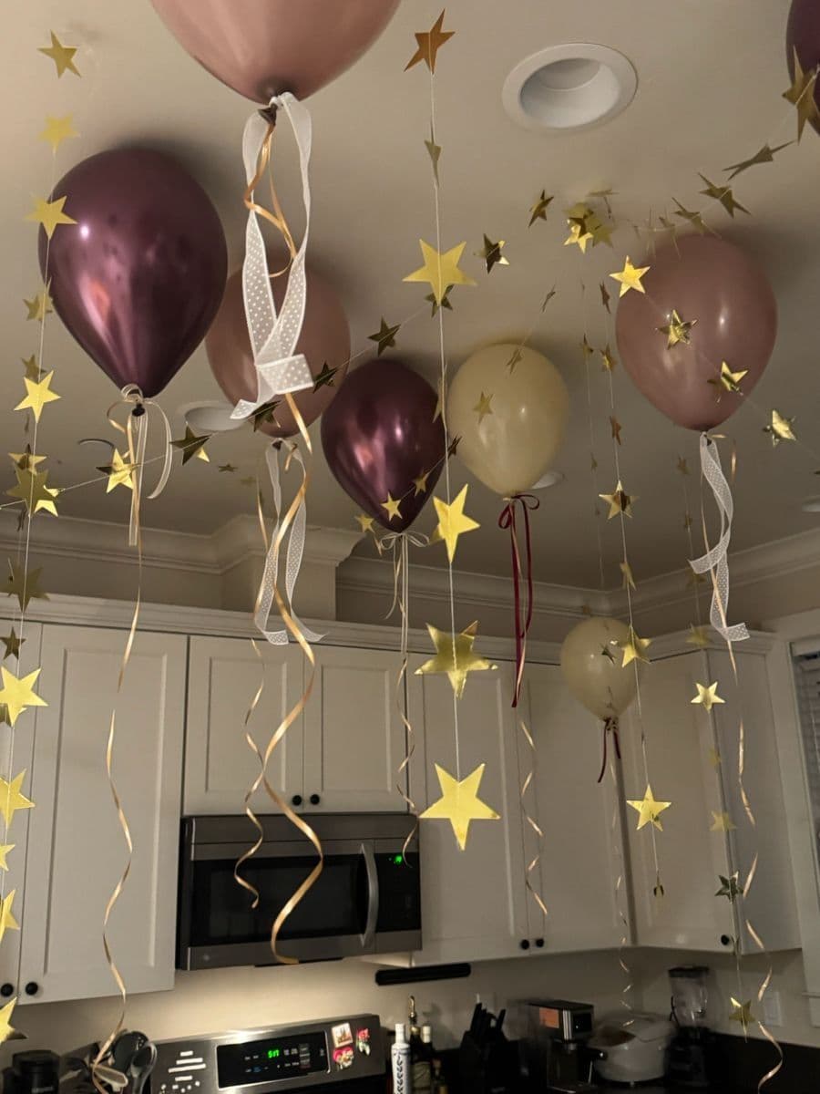 Surprise at-home birthday setup with chrome balloons and gold star garlands floating at the ceiling